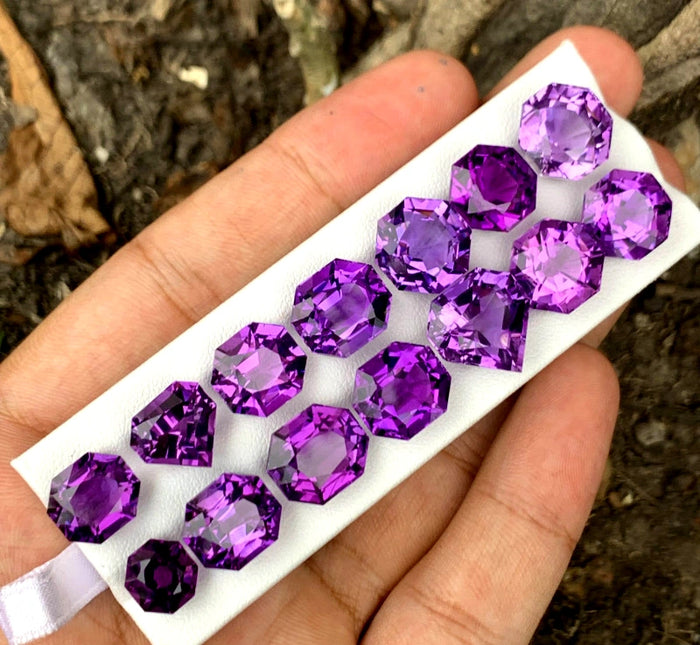 A collection of cut amethyst gemstones displayed on a white surface, held in a person's hand.