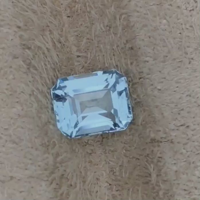 An octagonal cut 1.05 ct Aquamarine gemstone with a sea blue color, placed on a furry surface.