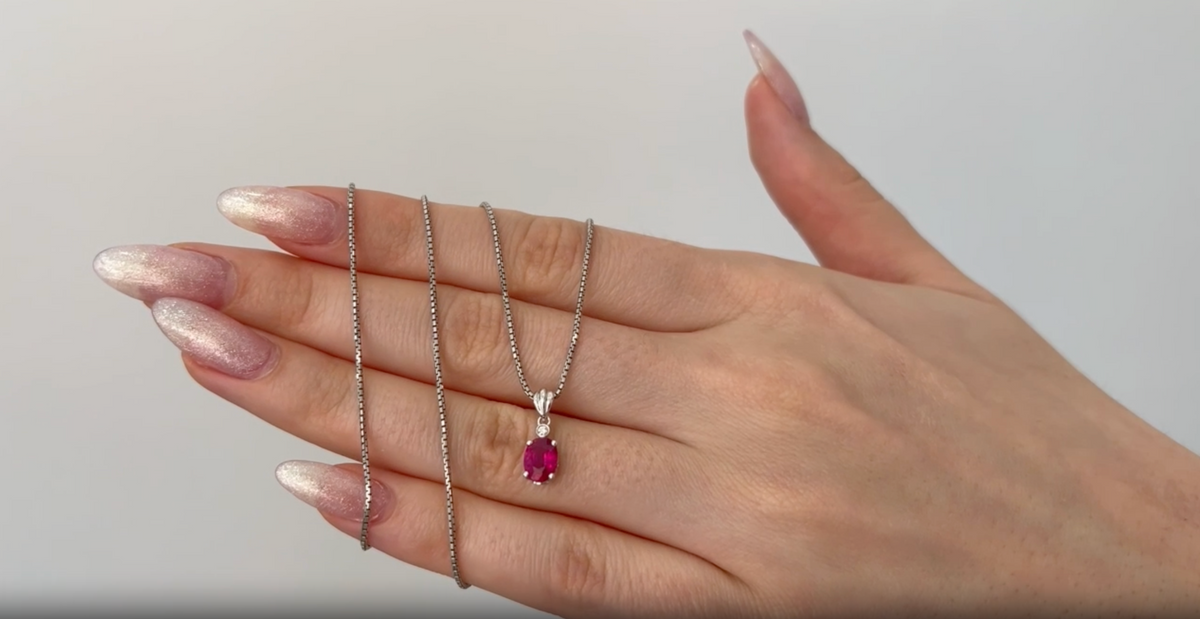 0.80 ct natural ruby pendant with diamond in 18K white gold, shown on a delicate chain and worn on a hand