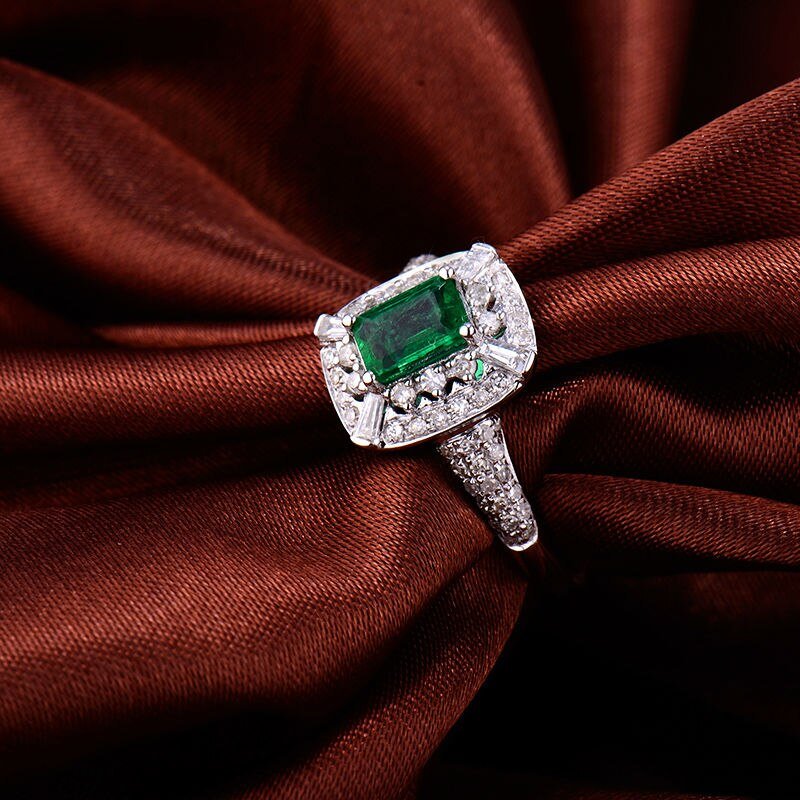 Natural emerald and diamond ring in 18K white gold displayed on luxury fabric